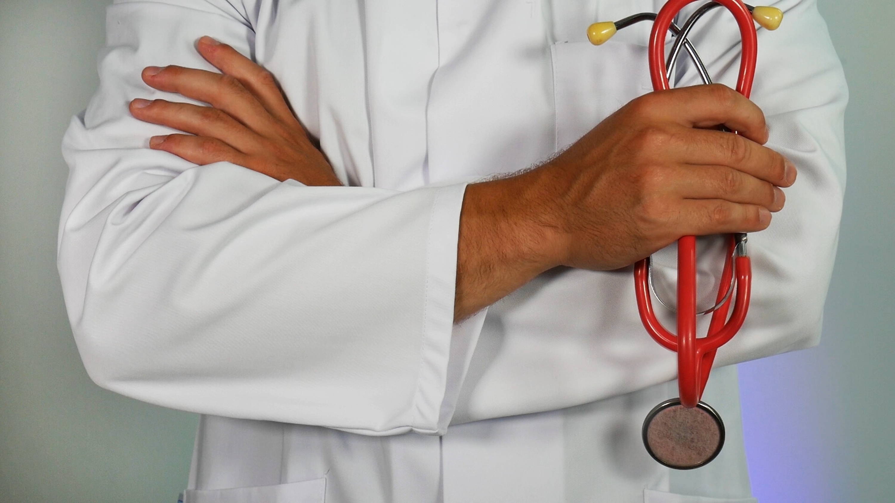 The chest of a doctor stands with arms crossed in front and holding a stethoscope.