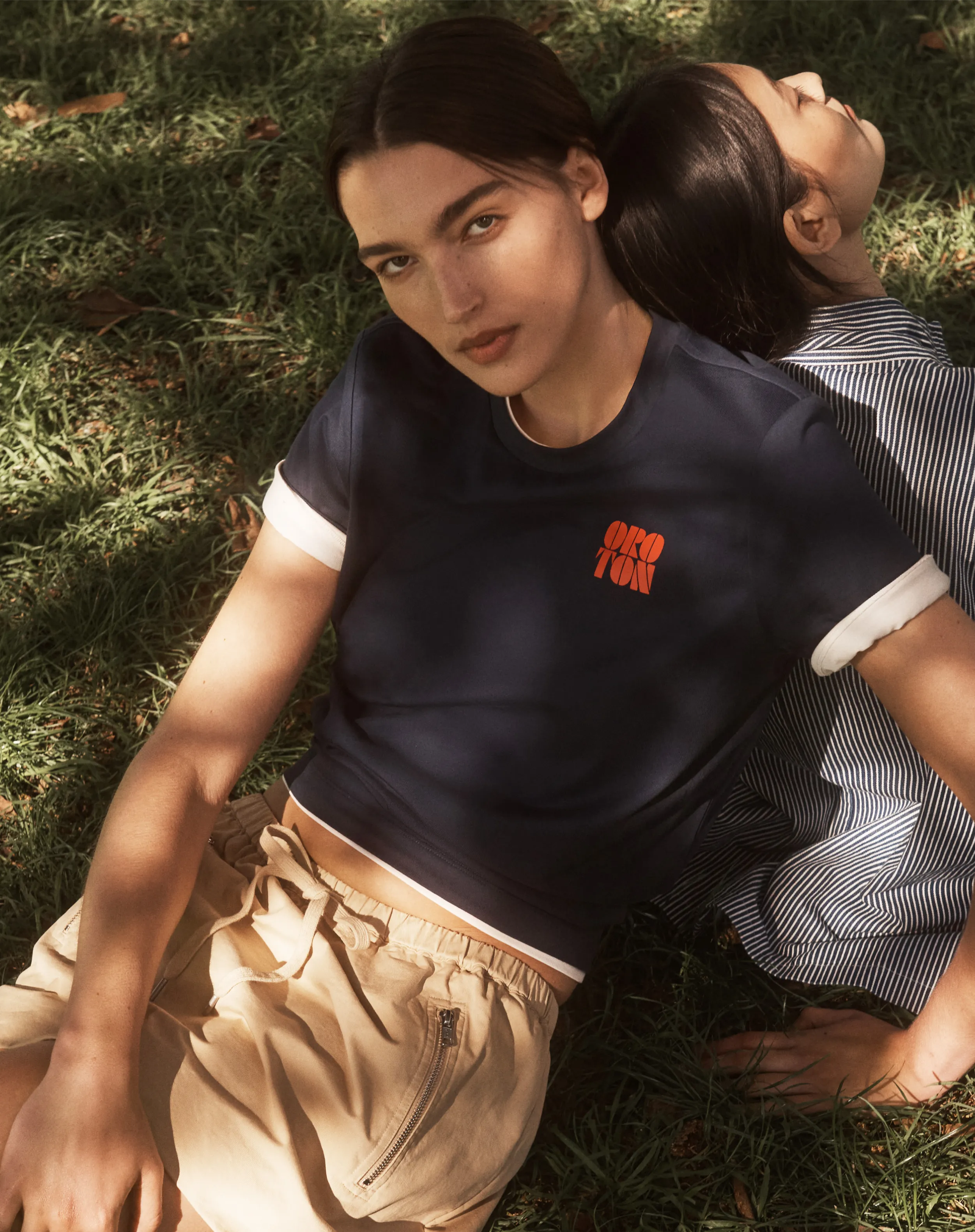 Two young women sitting on grass, one wearing a dark shirt and shorts.
