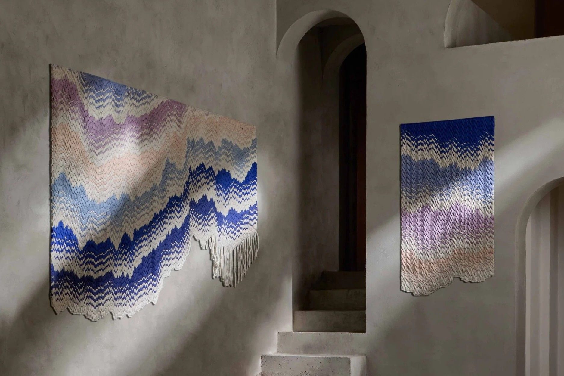 Two abstract wall tapestries on a wall with stairway.