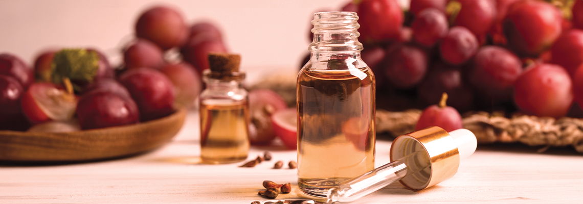 Bottles of oil in front of grapes on a table.