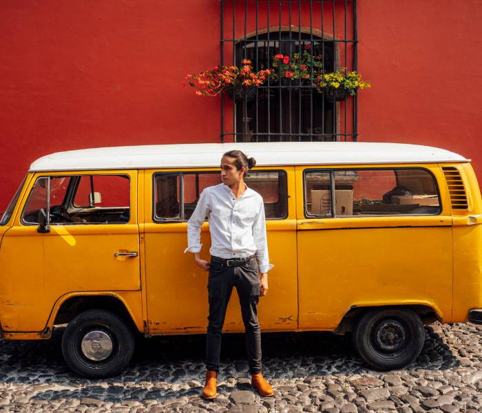 Man standing in front of yellow van wearing a white button down, dark pants, and caramel Mendozas