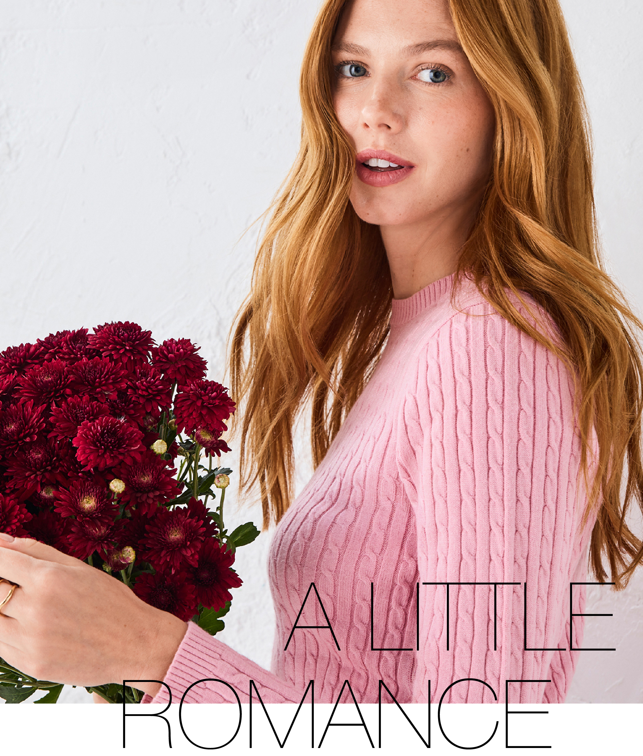 Woman in a pink sweater holding a bouquet of red flowers.
