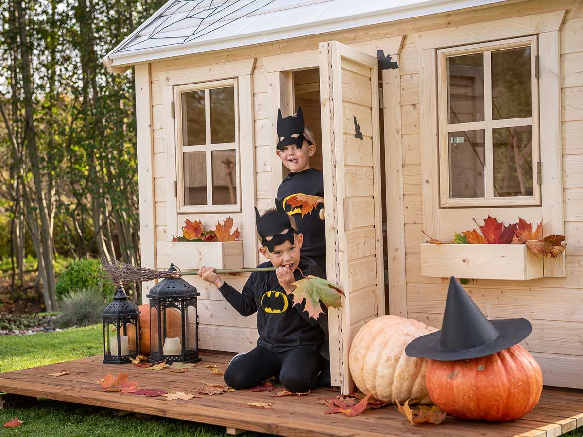 Two boys play on the terrace of an outdoor playhouse decorated for Halloween by WholeWoodPlayhouses