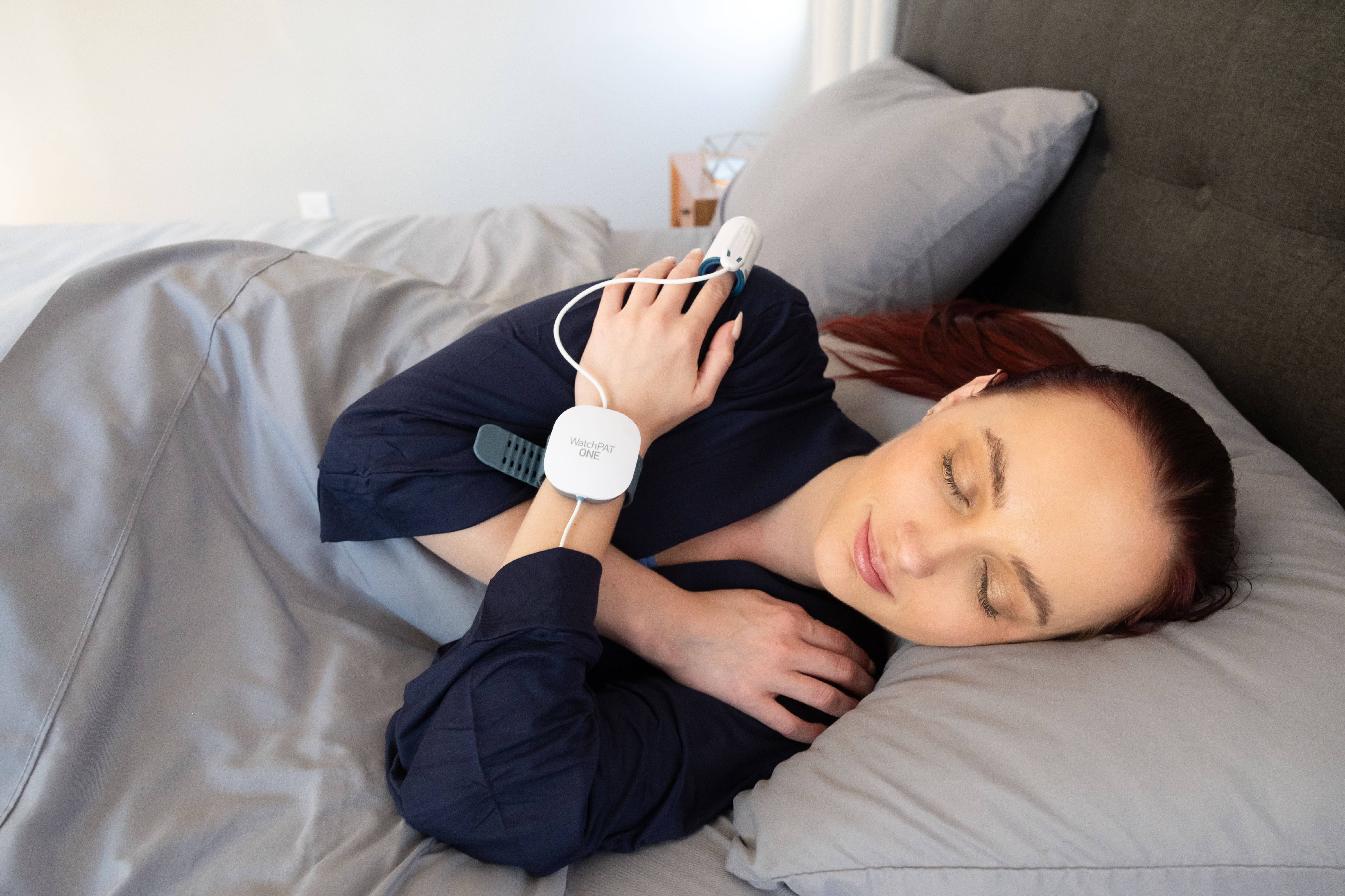 Person sleeping in bed, wearing a smartwatch and holding a phone.