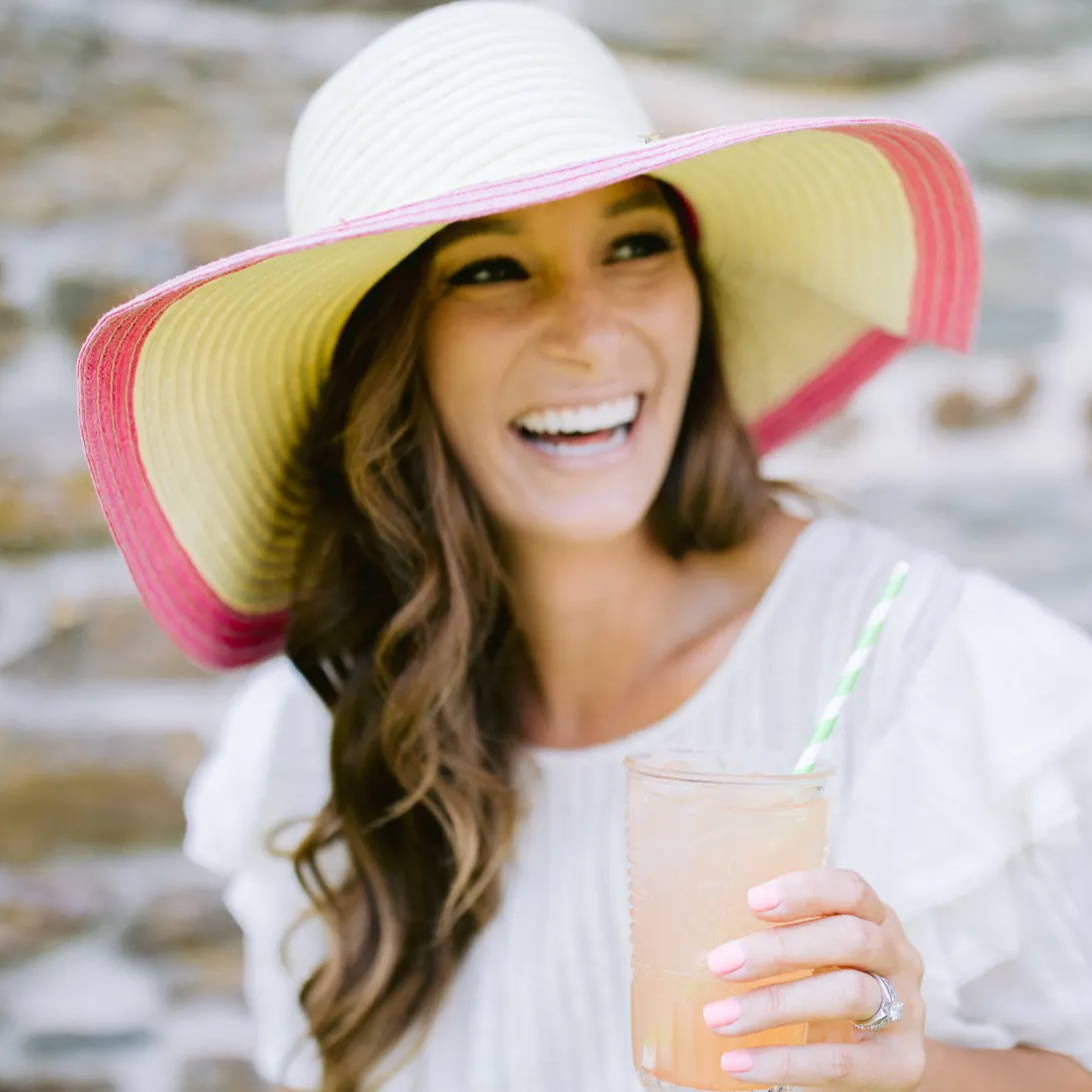 WOman at beach wearing large white wide-brimmed hat drinks True Lemon Pink Lemonade