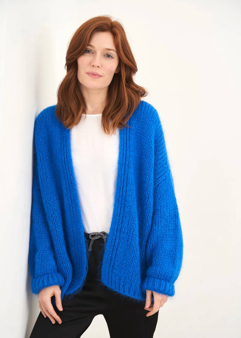 A model wearing a blue knitted oversized cardigan over a white top and black trousers