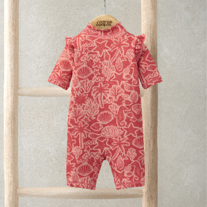 Red floral-patterned baby romper hanging on a wooden rack.