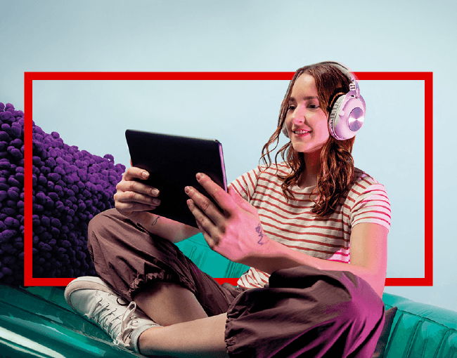 Persona joven sentada con auriculares y una tablet en un entorno colorido, destacando una campaña de Oktubre para las ofertas de tecnología. 