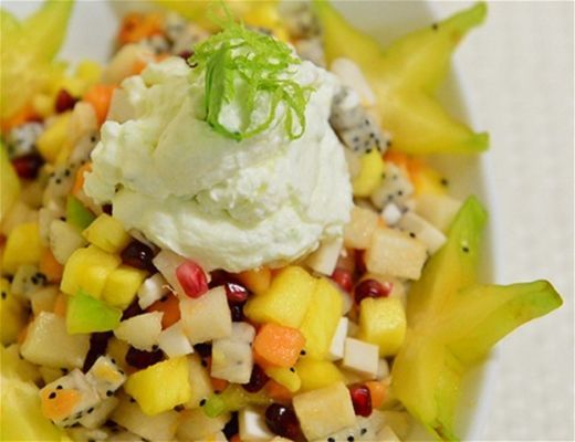 A colorful fruit salad with a scoop of cream and garnished with green.