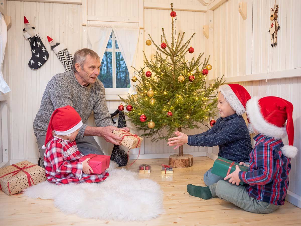 Grandfather with his grandchildren is inside of a decorated wooden playhouse by WholeWoodPlayhouses