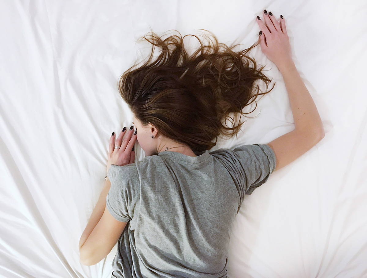 Brunette woman in a gray t-shirt sleeping face down on a bed.