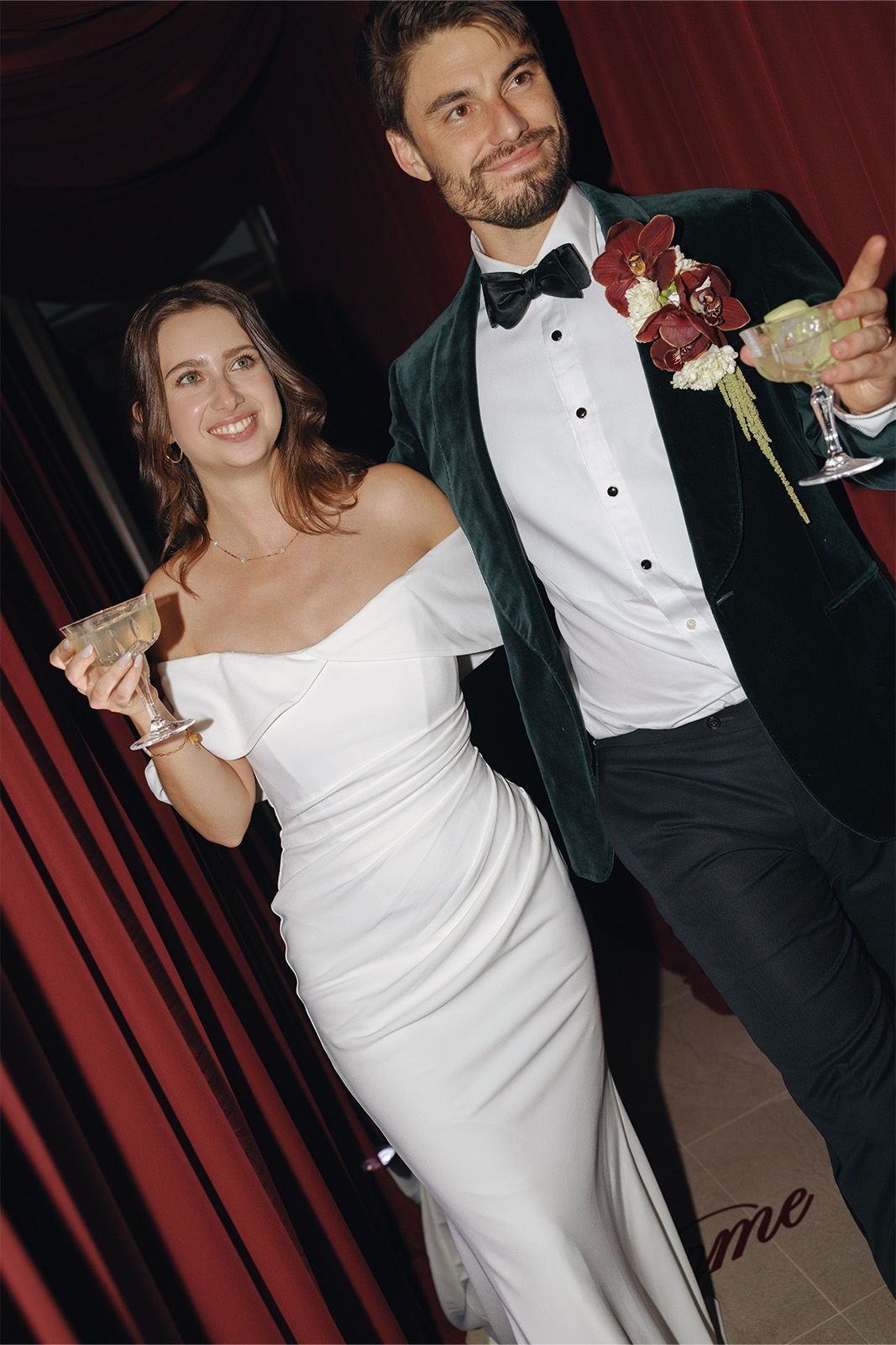 Couple dressed elegantly, smiling, walking together with drinks and flowers.