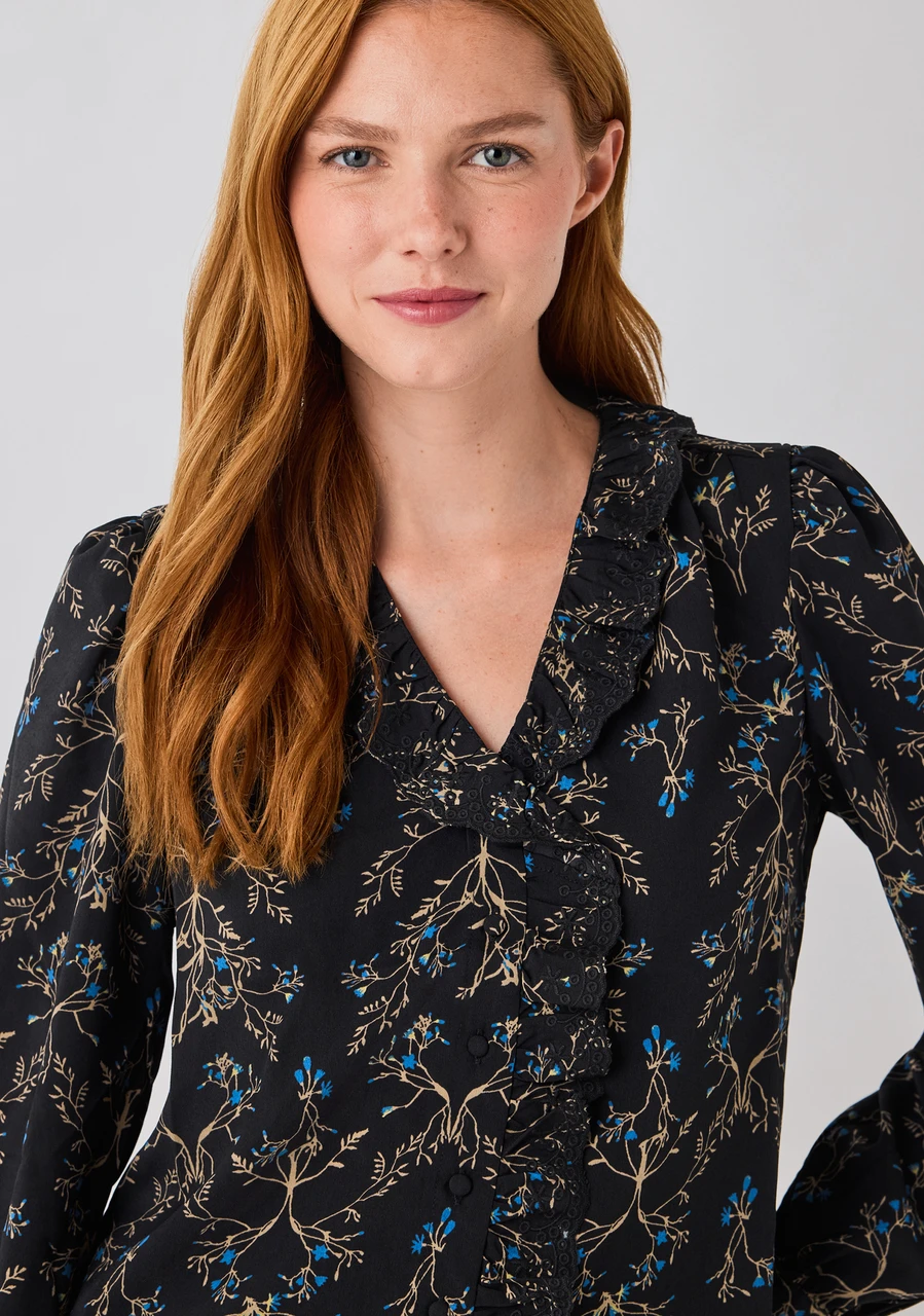Woman with long red hair wearing a floral-patterned blouse.