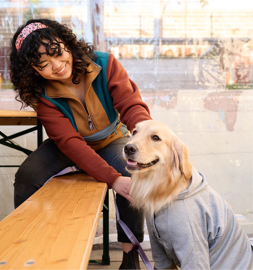 Person sitting on a bench with a golden retriever wearing a hoodie.