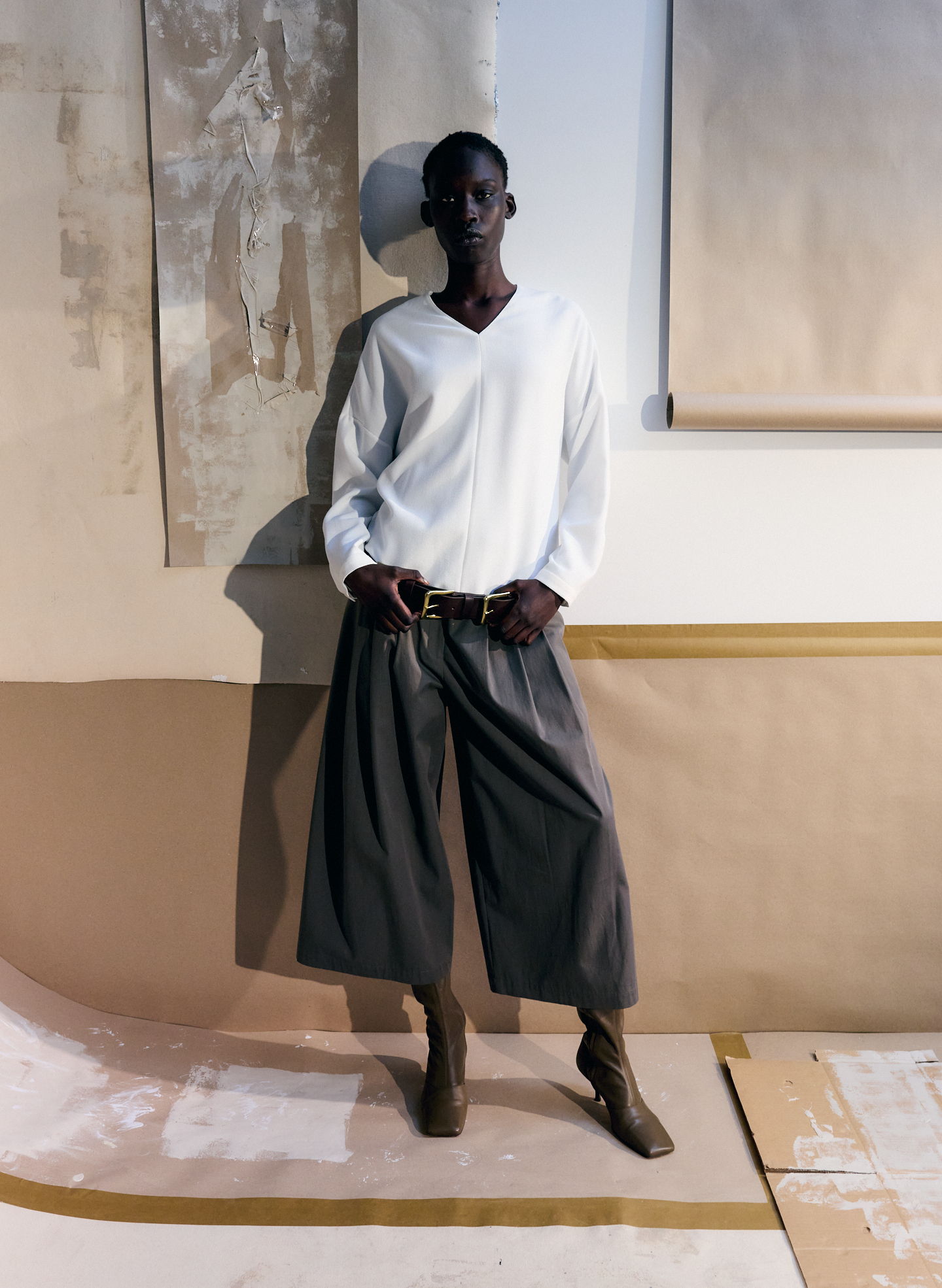 Person wearing a white top and wide gray pants, posing in an artistic setting.