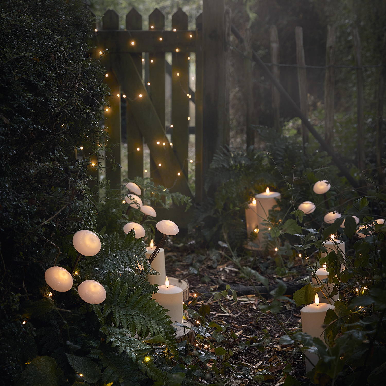 Des balises solaires en forme de champignons, des bougies d'extérieur et des guirlandes lumineuses pour une déco enchantée dans le jardin. 