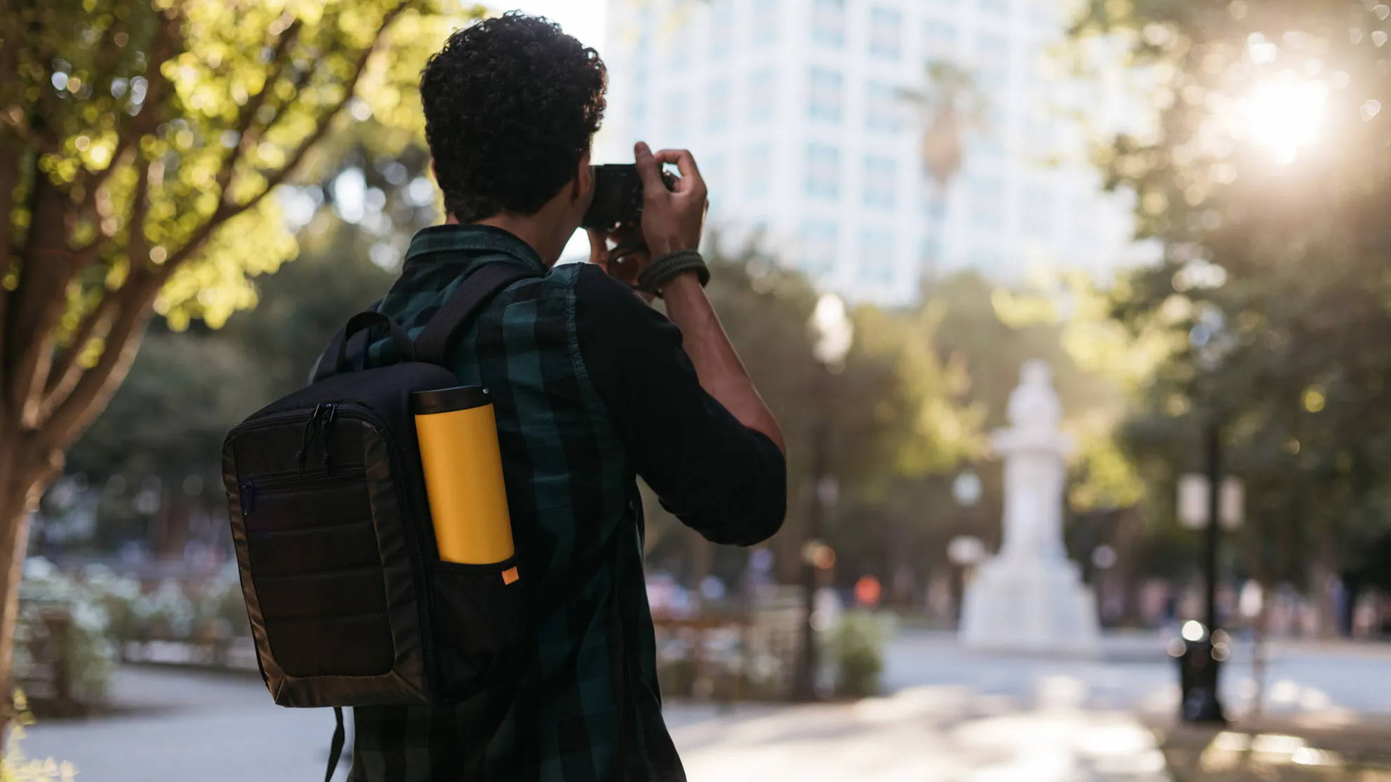 man taking photos with a black backpack and a marigold klean kanteen