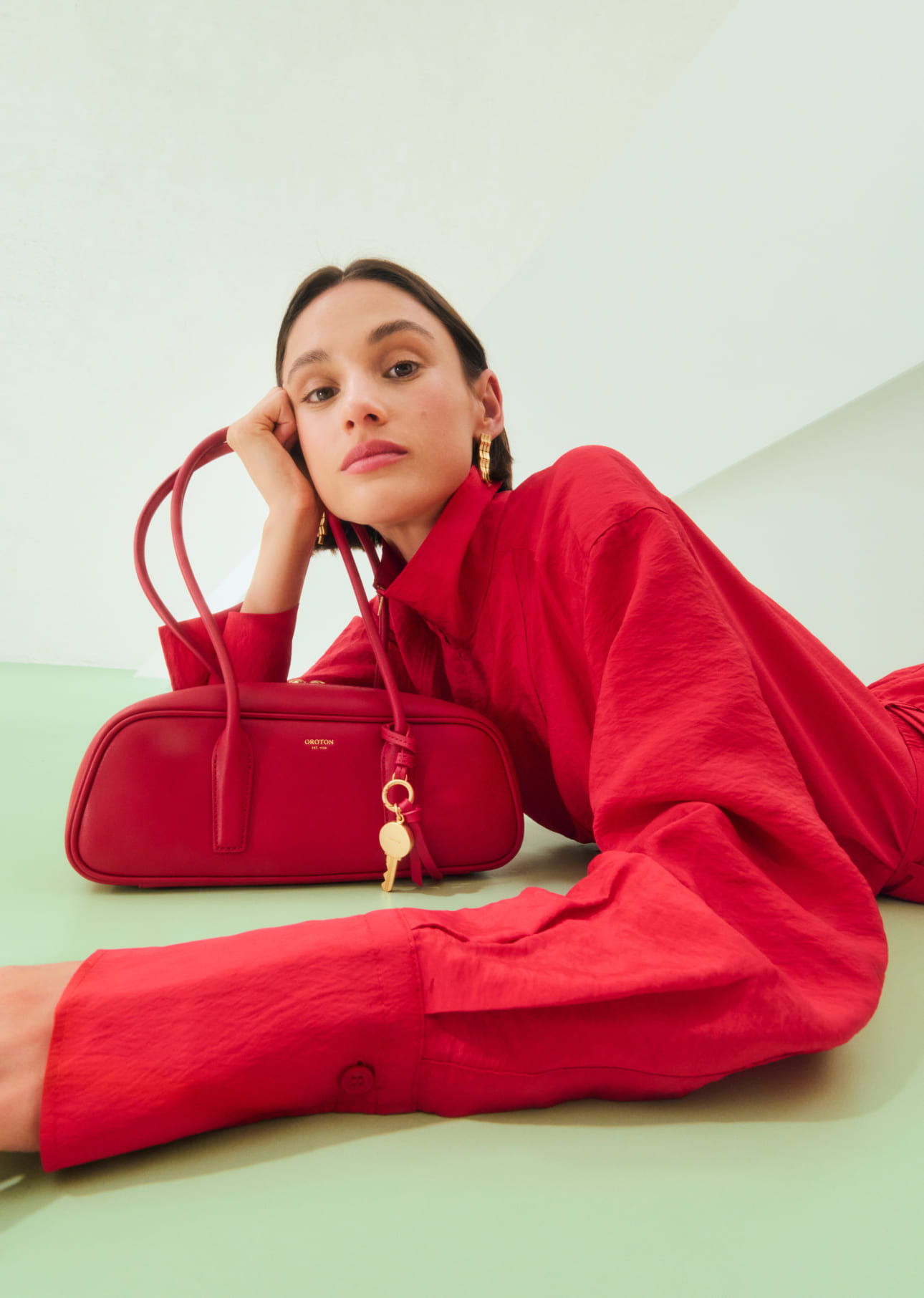 Woman in red shirt poses with a red handbag on a green surface.