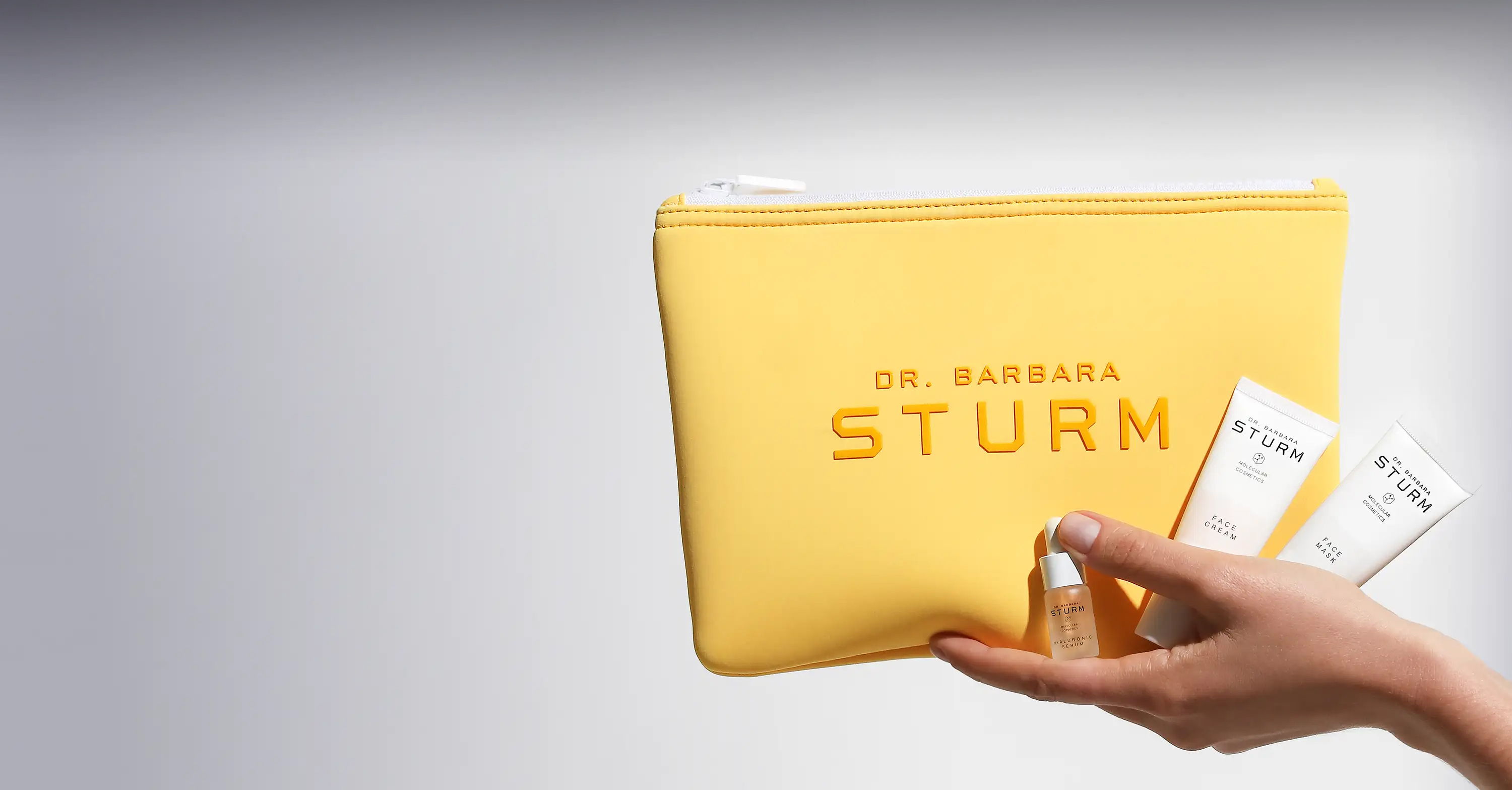 A hand holding a yellow pouch and skincare products.