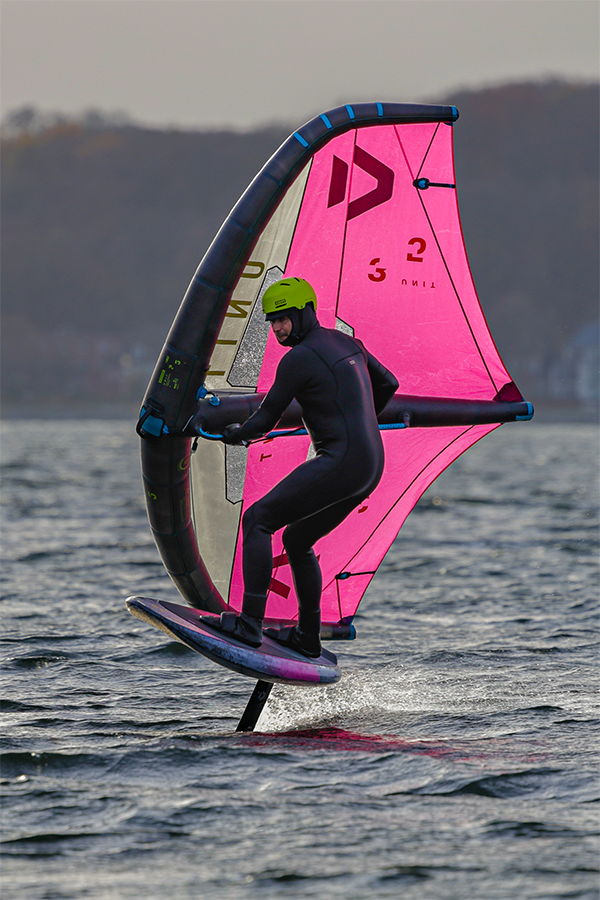 Person windsurfing on a body of water with a pink sail.