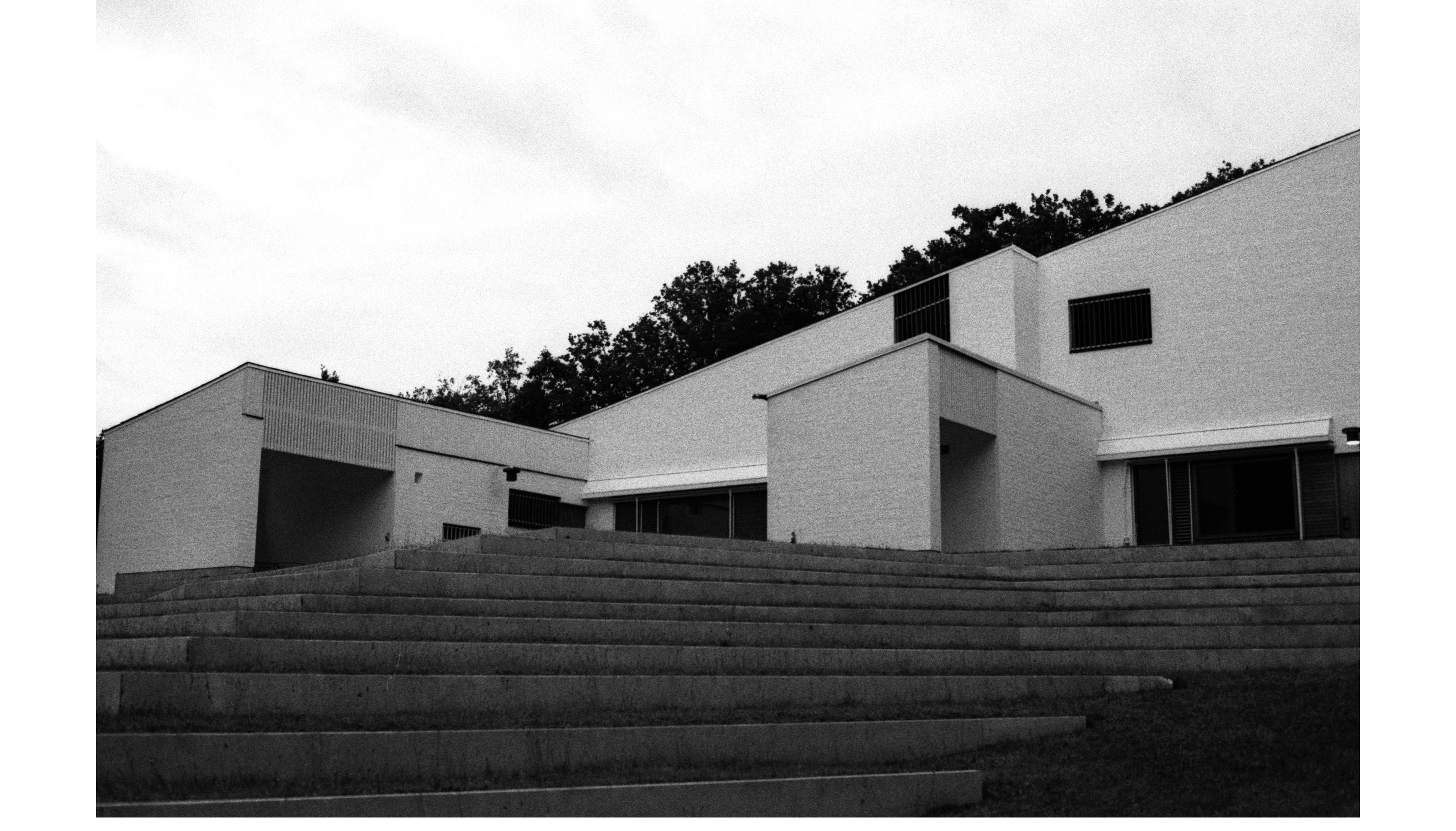 Modern architectural structure with steps, trees, and a cloudy sky.