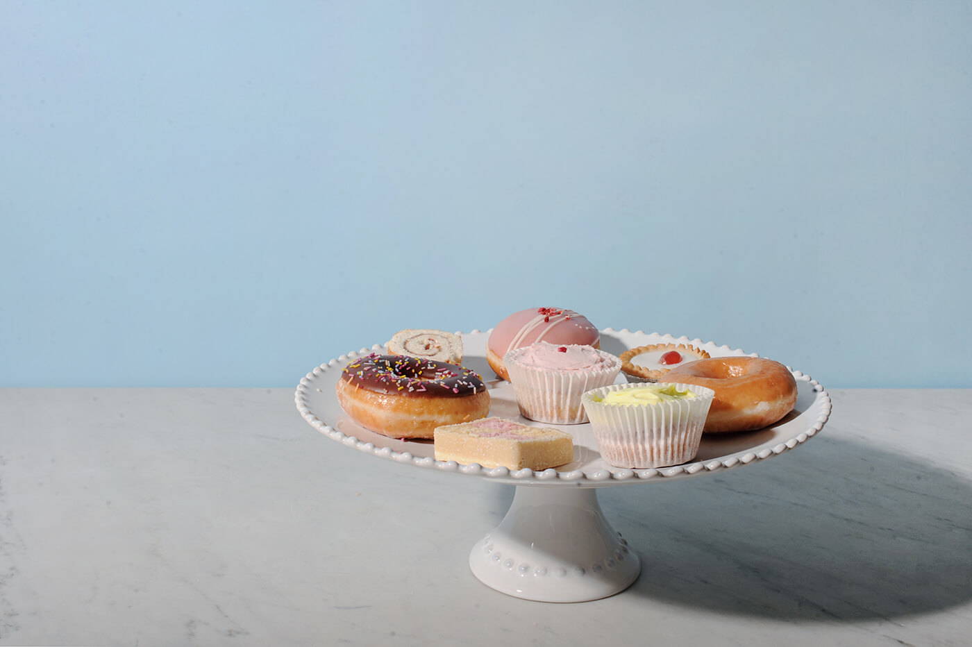 A Costa Nova Pearl White Cakestand on a marble table, filled with cakes and donuts.