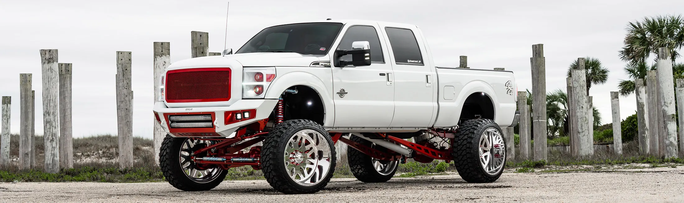 Corbin's lifted white 2016 Ford F250 Super Duty with red suspension and chrome wheels parked on a coastal gravel path
