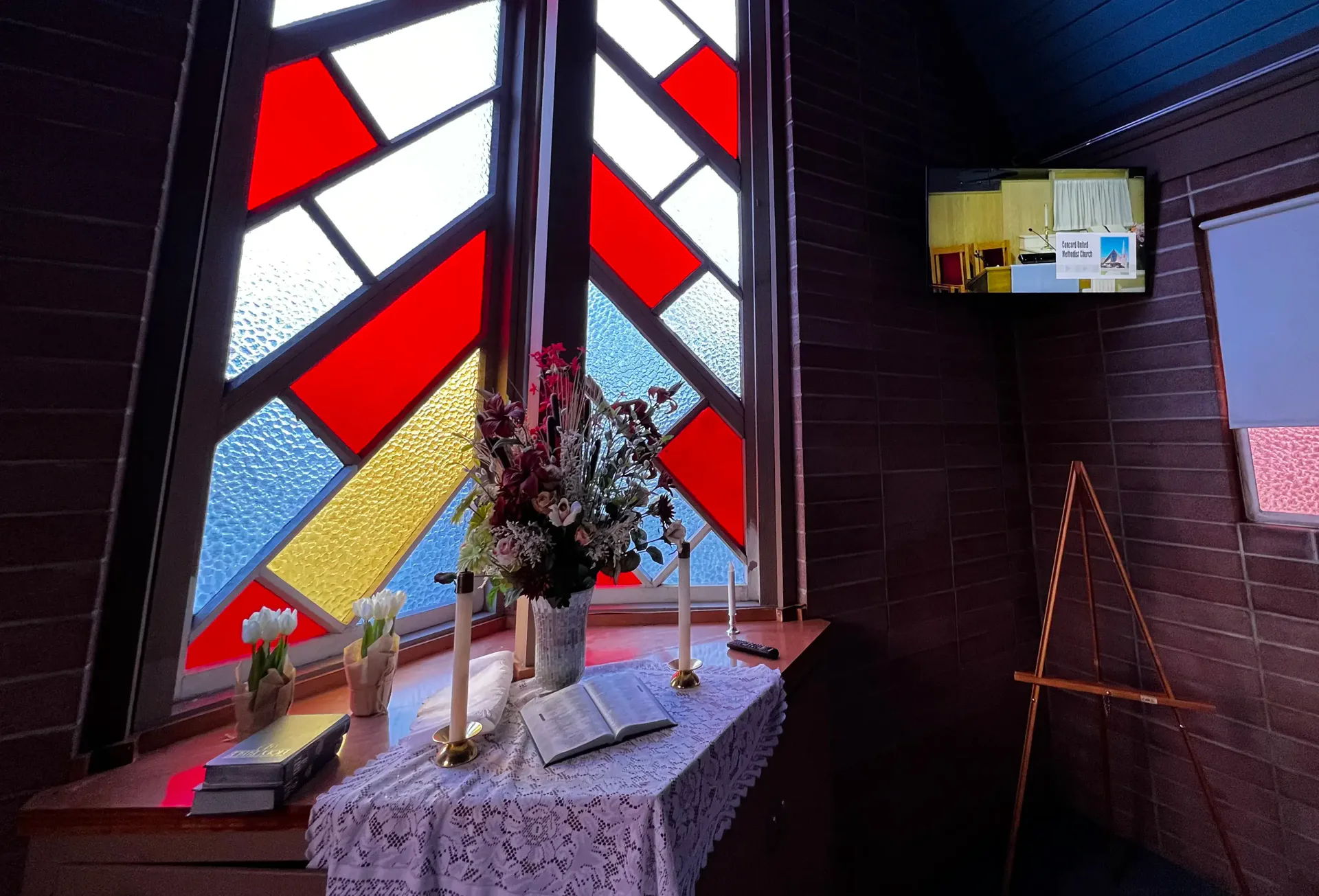 Interior of a chapel featuring stained glass, altar, and a television screen.