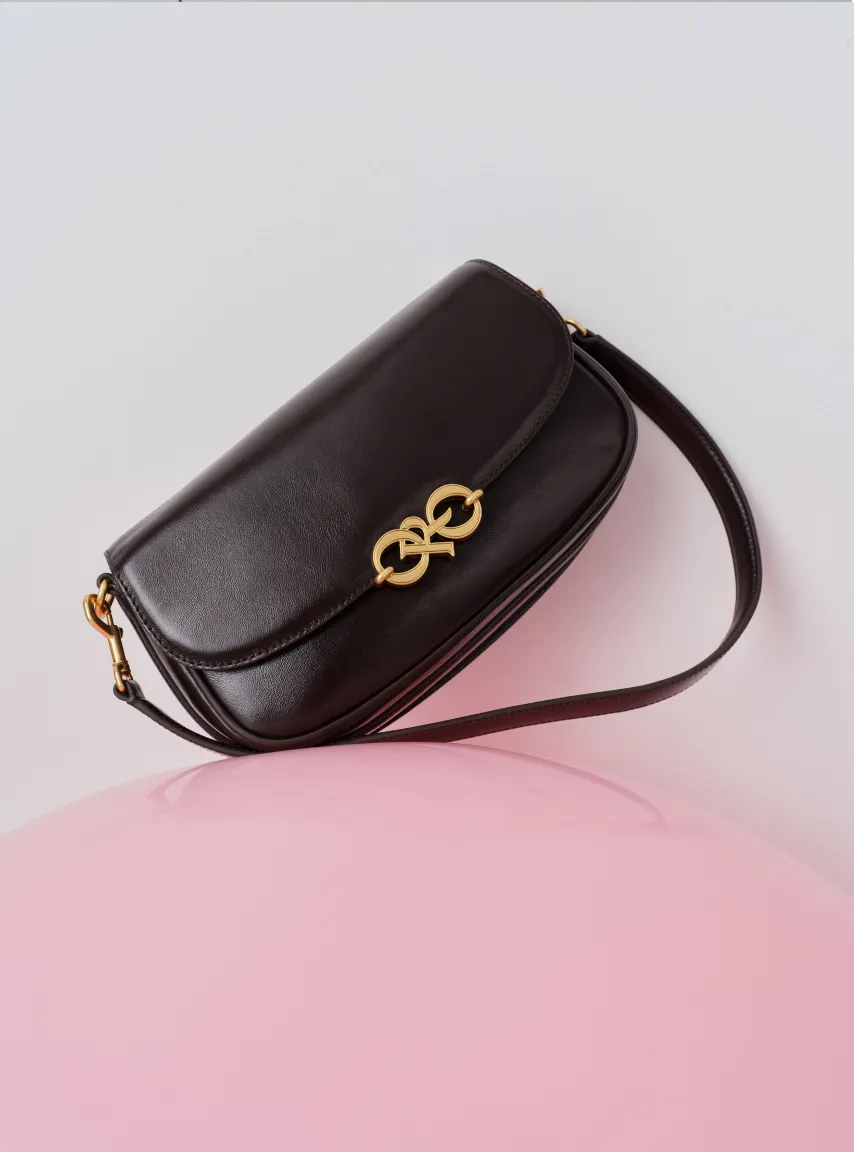 A black handbag with a gold clasp on a pink surface.