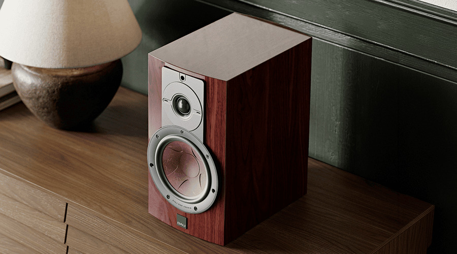 A wooden speaker on a table beside a lamp.