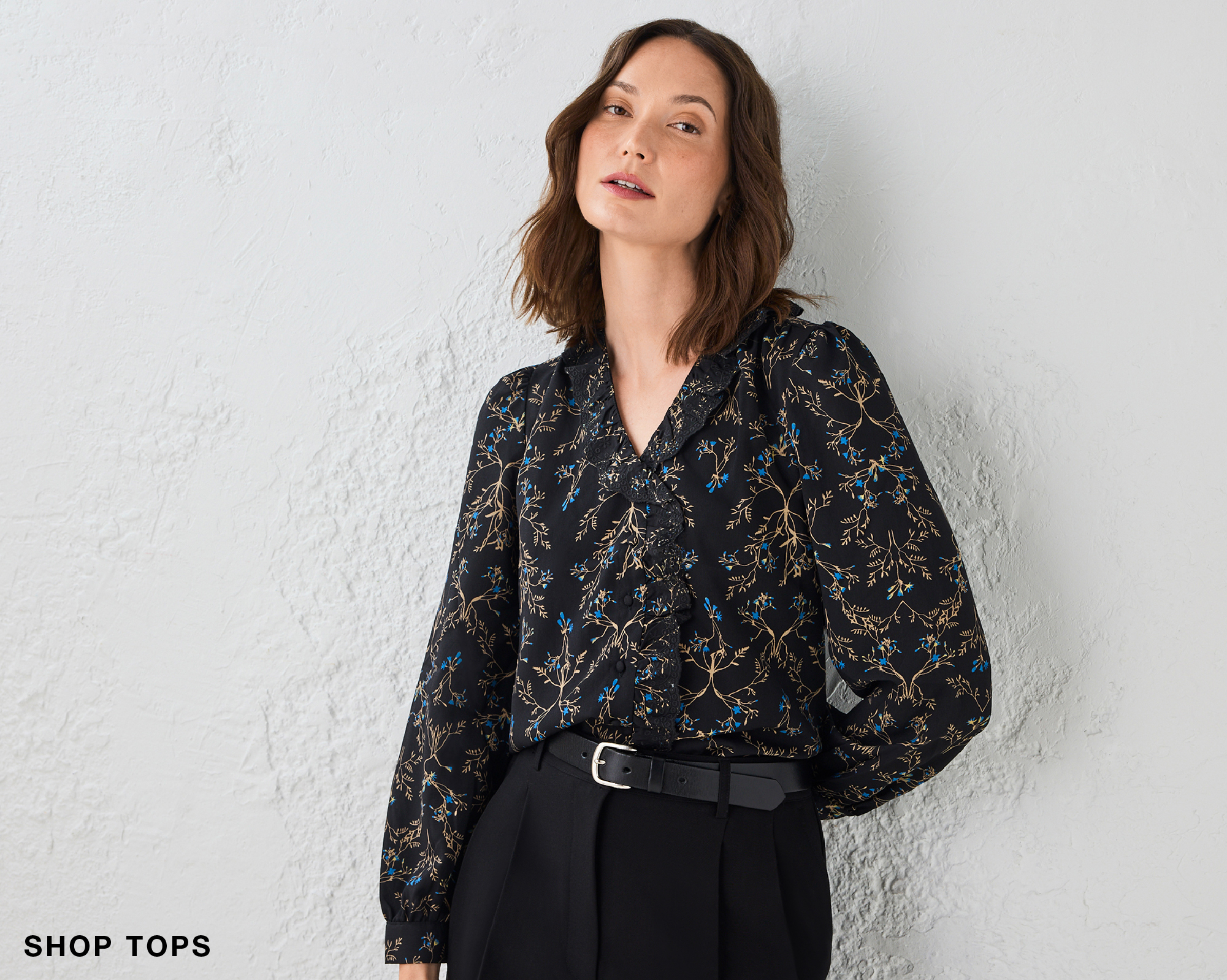 Woman in a patterned blouse posing against a textured wall.