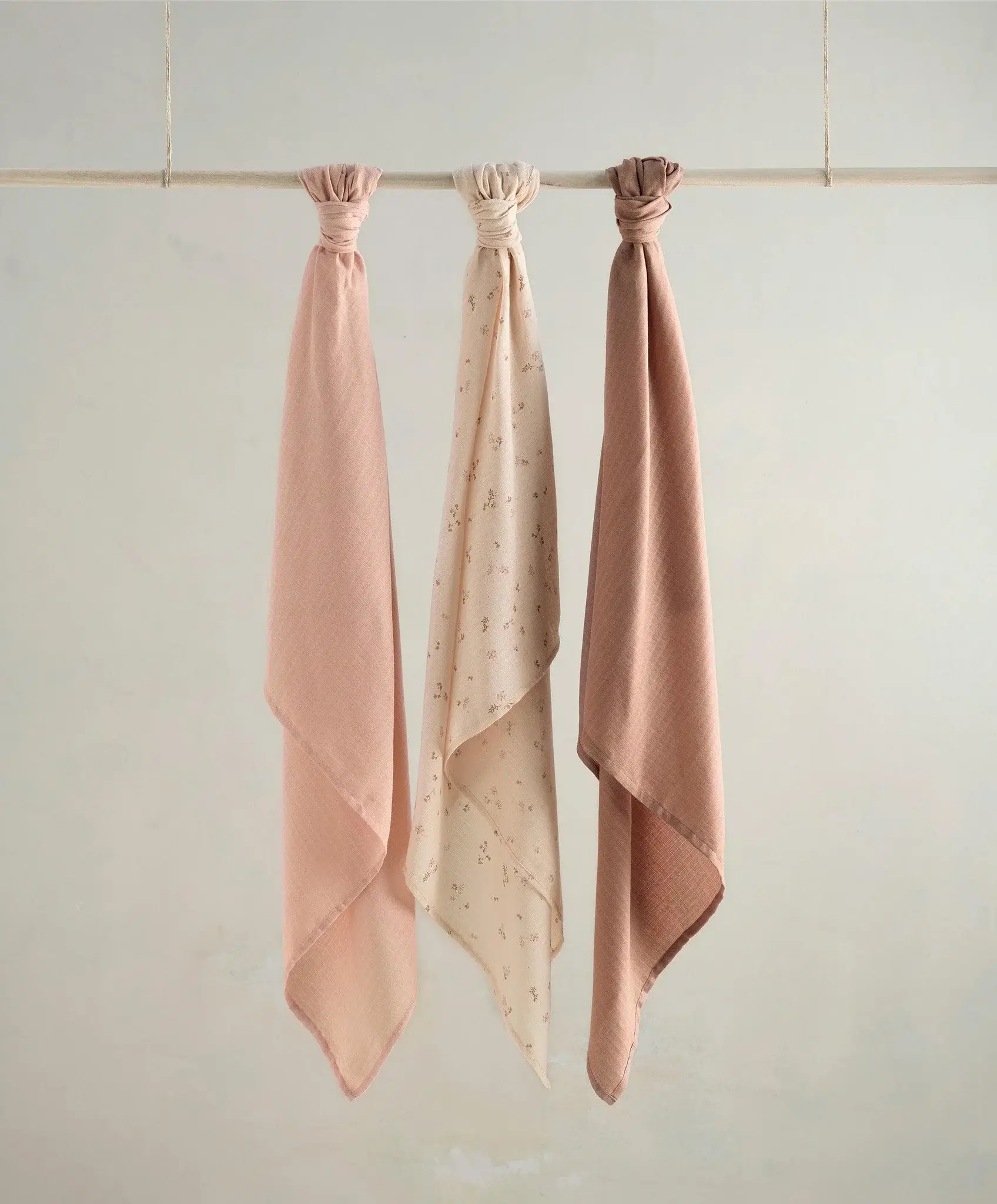 Three scarves in soft pink tones hanging on a line.