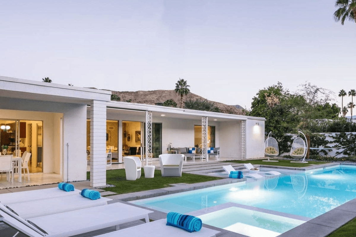 Modern home with a swimming pool, patio seating, and rolled blue towels placed on white loungers at dusk.