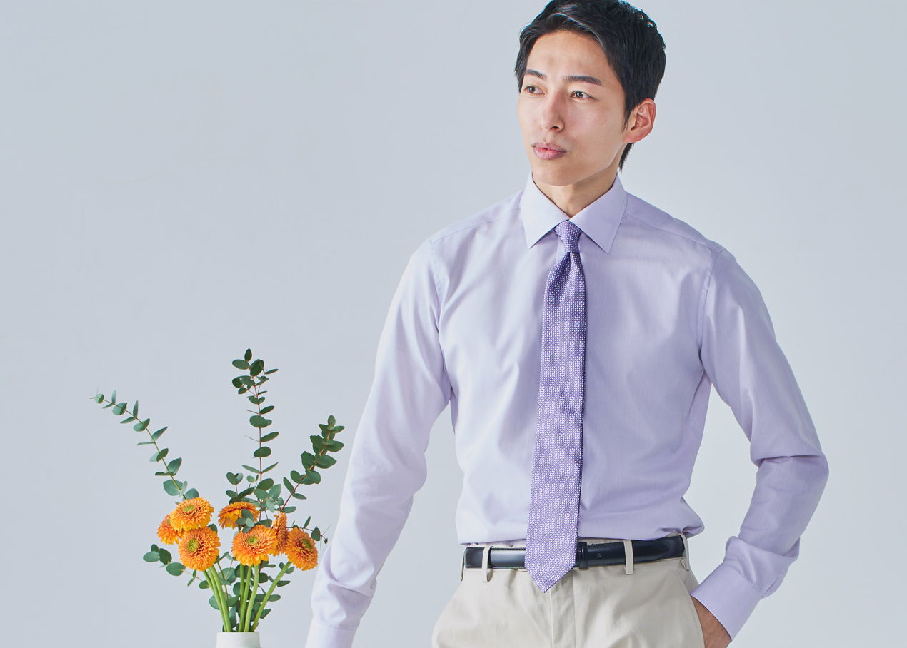 Man in a purple shirt and tie, standing next to a flower arrangement.