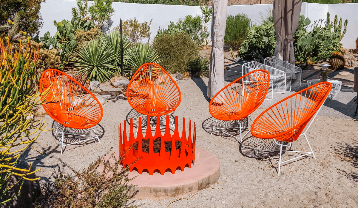 A desert patio featuring Royal fire pit with Acapulco chairs in bright orange. 