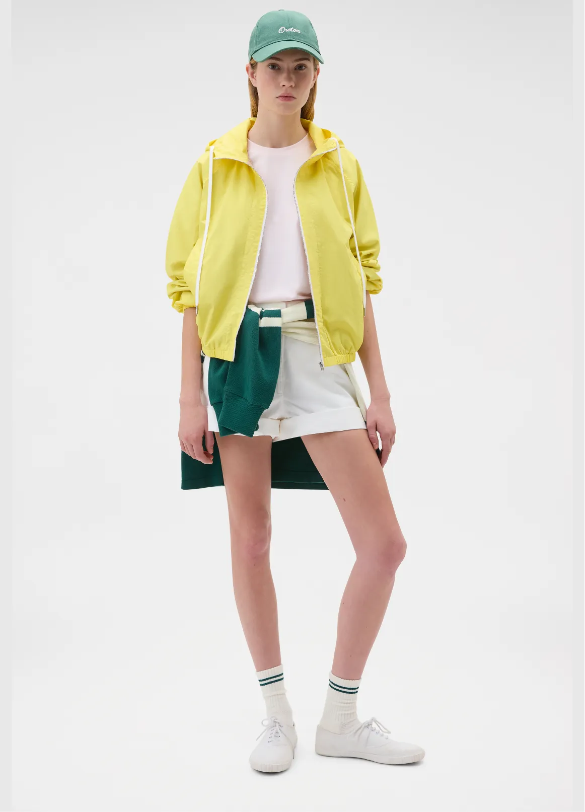 A person wearing a yellow jacket, white shirt, and green cap stands confidently.