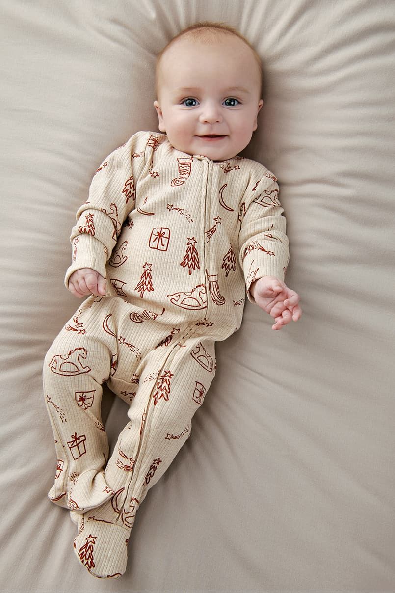 Baby in patterned pajamas smiling on a beige surface.