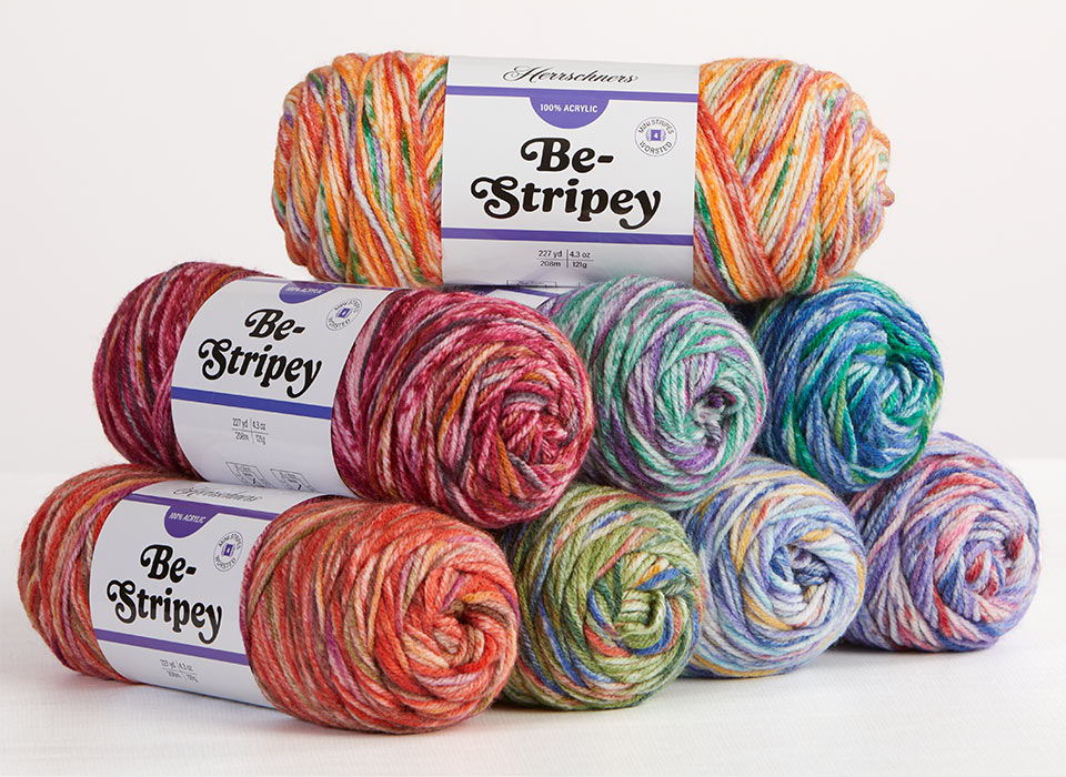 Colorful Herrschners Be-Stripey yarn skeins stacked with labels, showcasing various striped patterns.