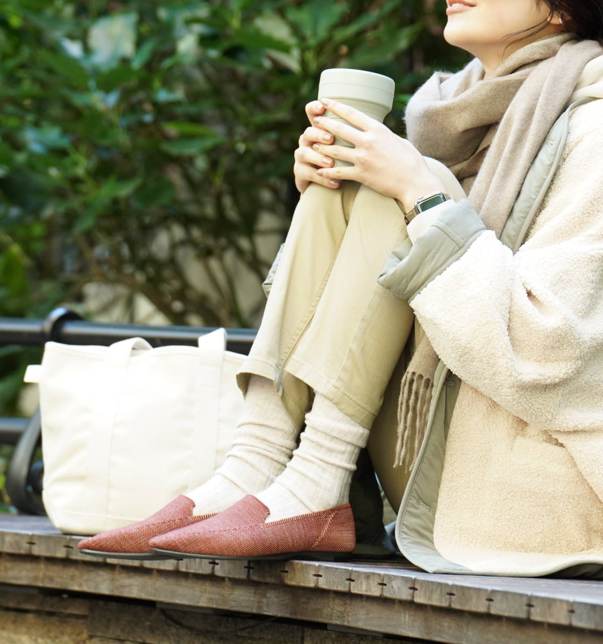 Hidamari Thermo Loafer（ひだまりサーモローファー）を履いて温かいコーヒーを片手にベンチに座る女性
