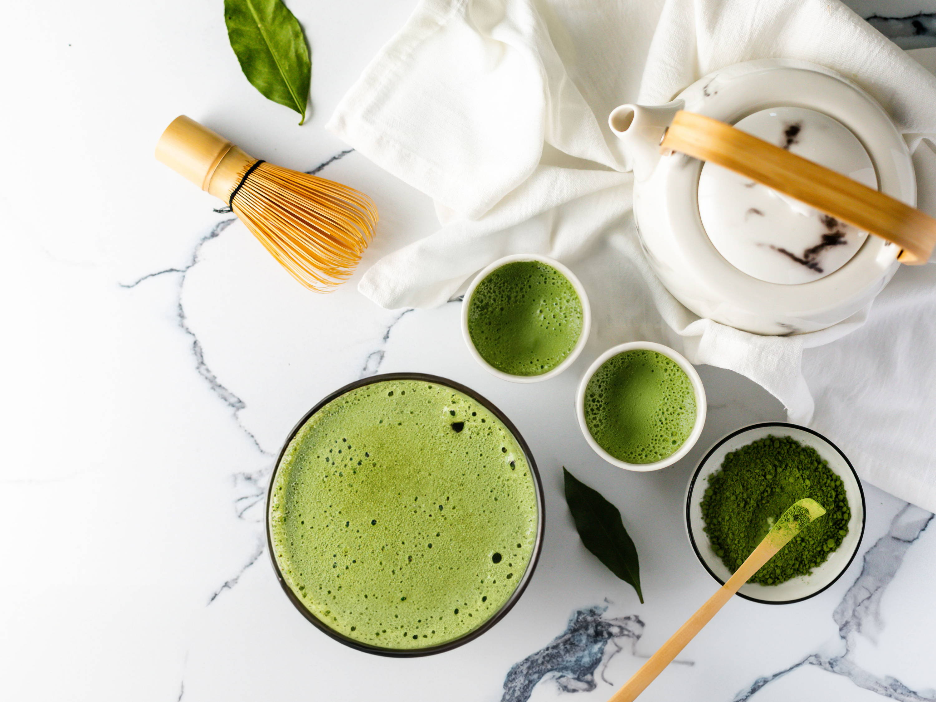 Aiya Matcha tea set with bowls, whisk, and green leaves on a marble surface.