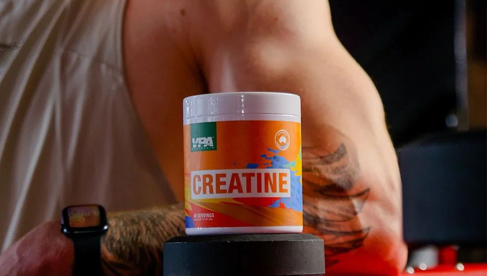 Container of creatine with a muscular arm in the background.