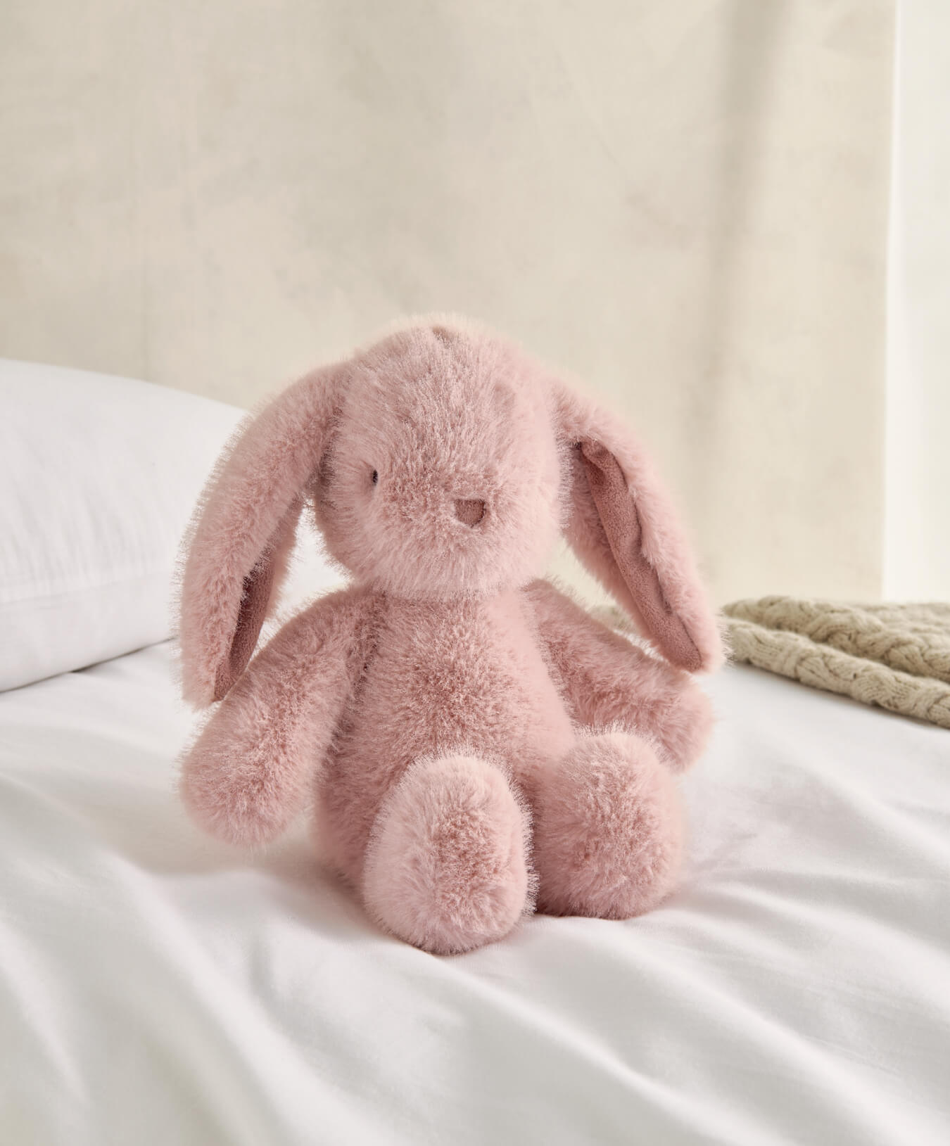 A soft pink stuffed bunny sitting on a bed.