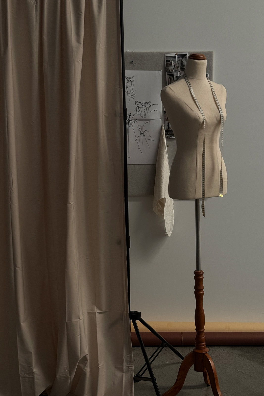 A dress form beside a curtain and design sketches on a wall.