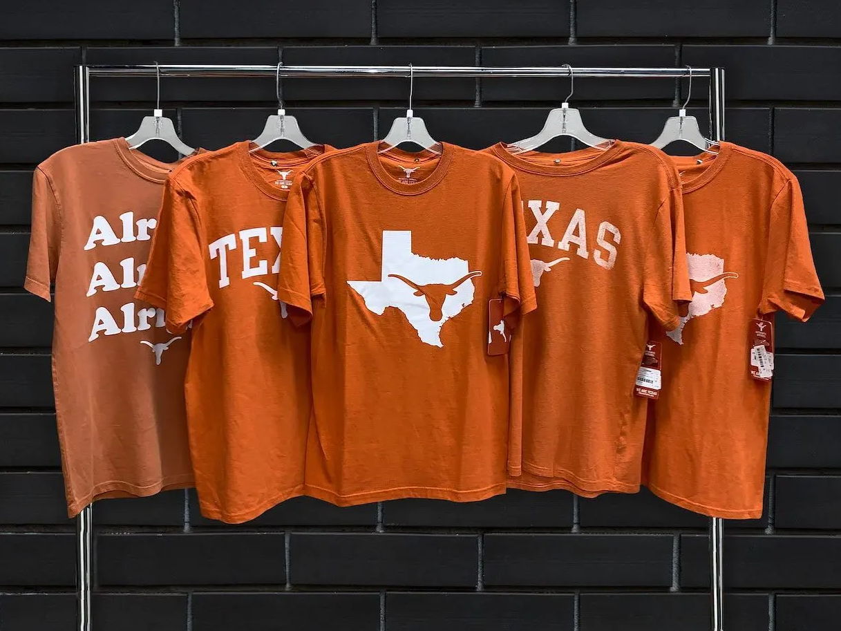 University of Texas apparel displayed on a rack infront of black brick wall