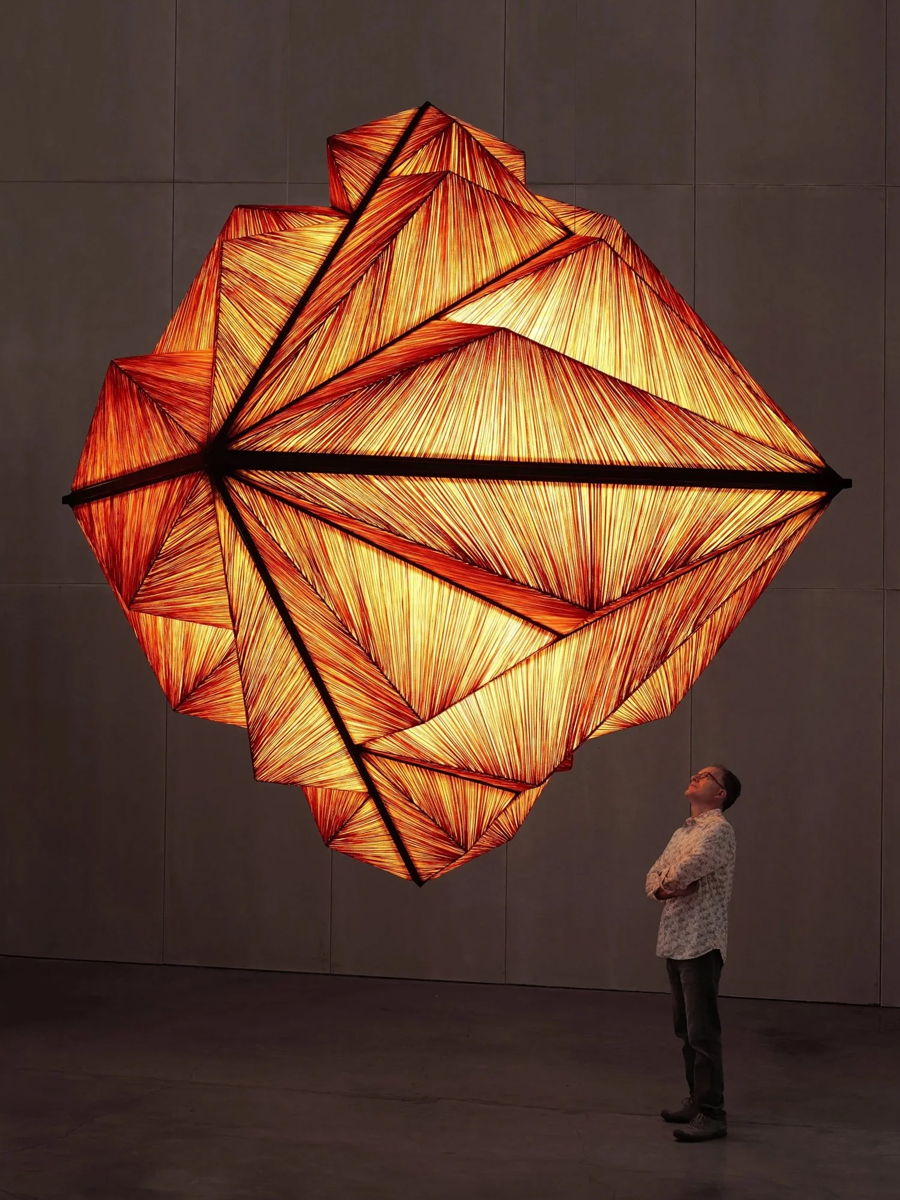 A person gazes up at a large, illuminated geometric sculpture.