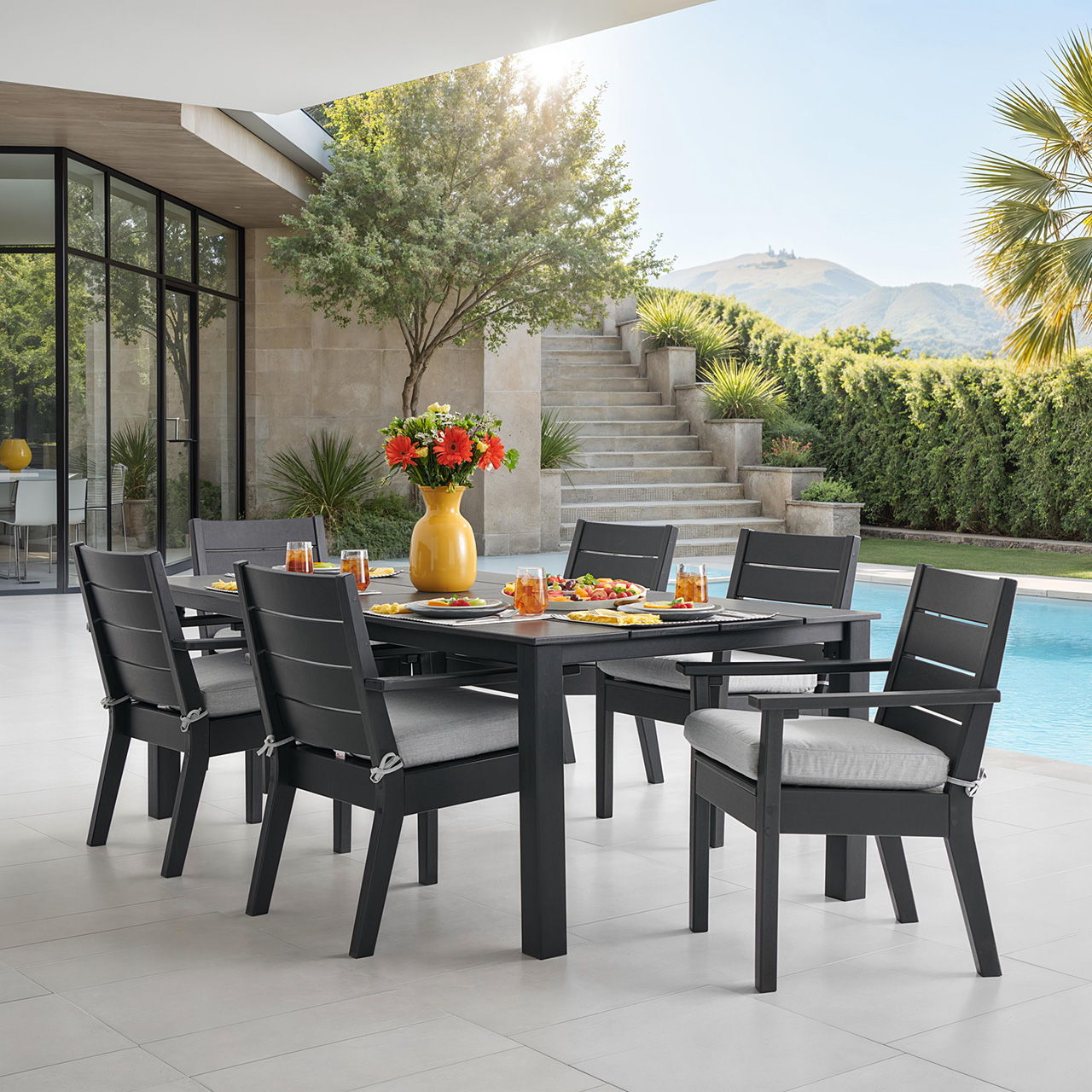 Outdoor dining set by a poolside with flowers and mountain view.