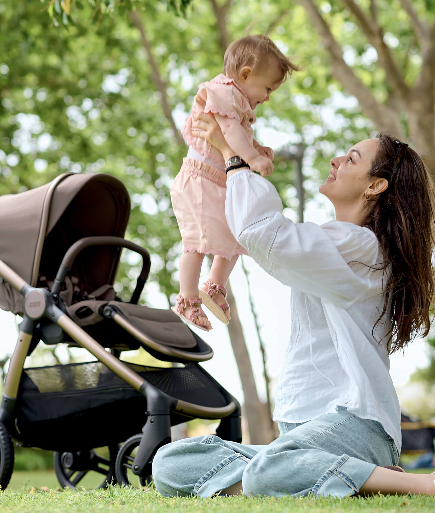Woman playing with a baby in a park near a stroller.