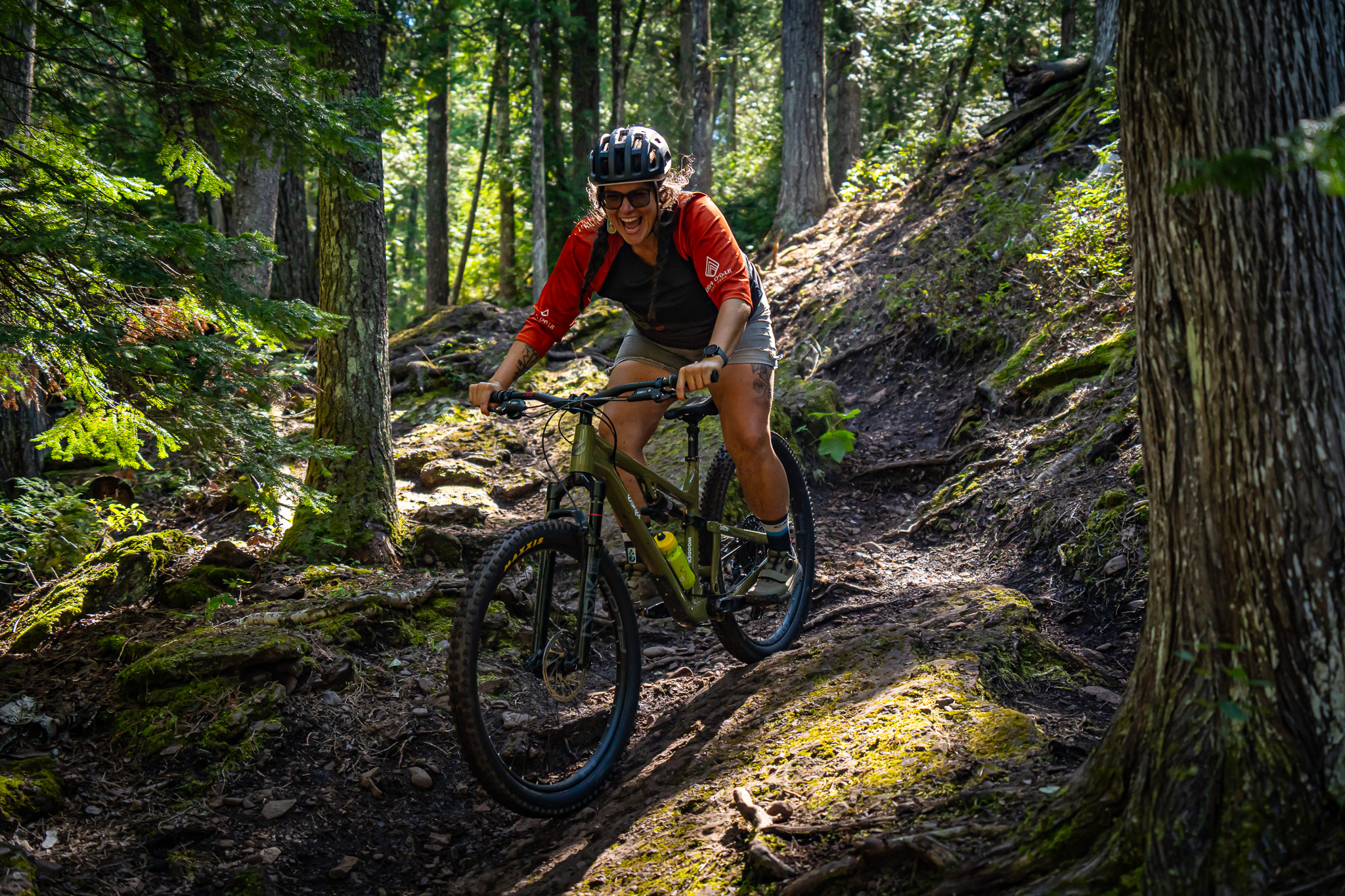 Mountain biker navigating a wooded trail in sunlight.