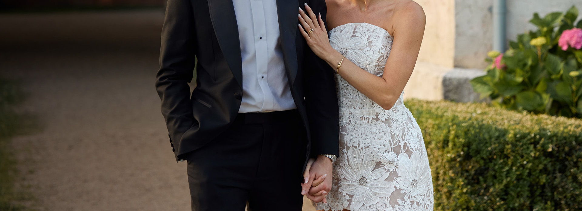 A bride and groom holding hands, dressed elegantly outdoors.