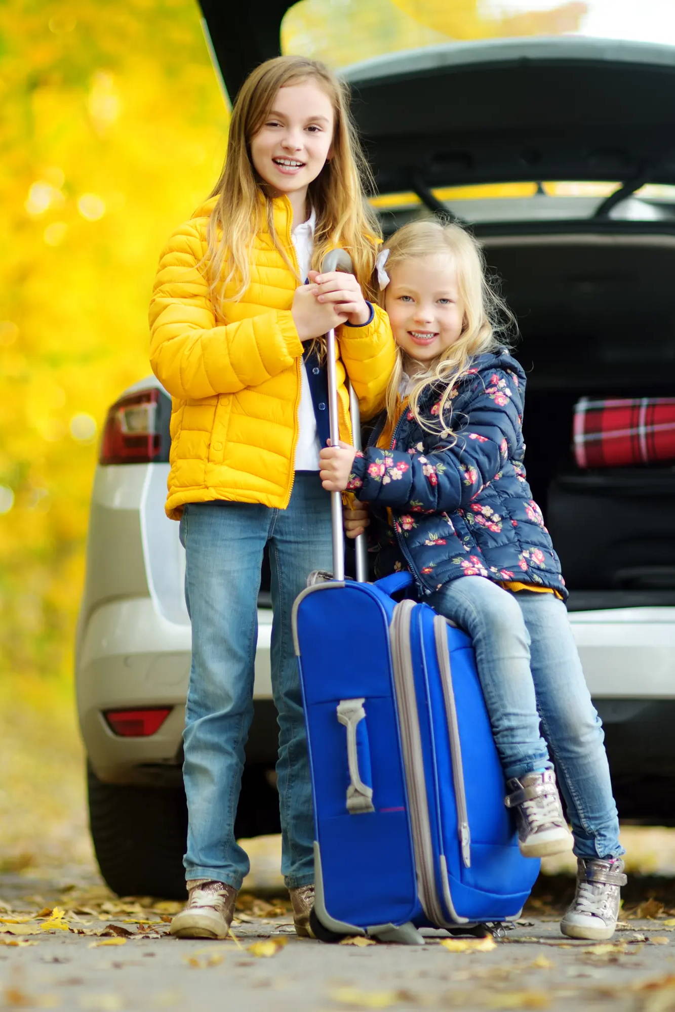 kids holding suitcase outside of car in the fall